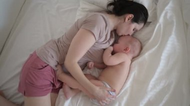 Genç anne, yeni doğmuş tatlı bir bebekle yatakta yatıyor. Çıplak erkek çocuğu kollarına alıyor, anne sütüyle sarılıp emziriyor. Sağlıklı çocuk, hastane kavramı ve mutlu annelik. Çocuk odası.