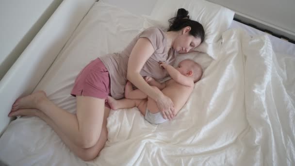 Müde Mutter liegt mit neugeborenem, süßem Säugling auf dem Bett, hält ihn auf den Armen, umarmt Stillen mit Muttermilch. Gesundes Kind, Krankenhauskonzept und glückliche Mutterschaft. Kinderzimmer — Stockvideo