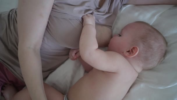 Молодая мать лежит с новорожденным милым голым младенцем на кровати, держит его на руках, обнимает и кормит грудным молоком. Здоровый ребенок, концепция больницы и счастливое материнство. Детская комната — стоковое видео