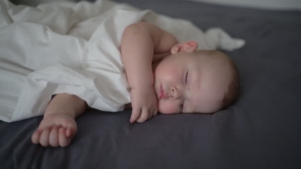 かわいい新生児 白いシートで覆われ 灰色のベッドの上で寝て — ストック動画