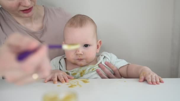 갓 태어난 어린아이는 재미있게 채소나 과일 가루를 숟가락으로 유리병에서 먹는 법을 배운다. 어린 어머니가 어린 아들 이 음식을 먼저 먹도록 도와 주는 모습. — 비디오