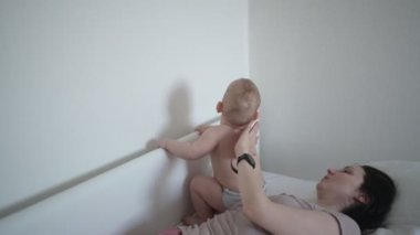 Mutlu genç bir anne, tatlı bir bebekle yatakta yatıyor, onu kollarına alıyor, sarılıyor ve sabahın erken saatlerinde oynuyor. Sağlıklı çocuk, hastane kavramı ve mutlu annelik. Çocuk odası.
