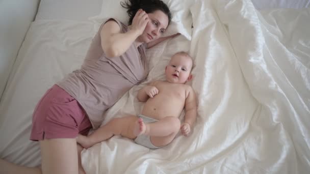 Glad ung mamma ligger med söta spädbarn småbarn pojke i sängen, hålla honom på armar, kramas och leka tidigt på morgonen. Friska barn, begreppet sjukhus och lycklig moderskap. Plantskola — Stockvideo