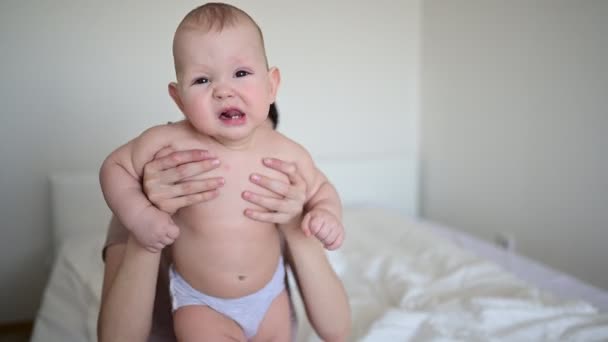 Schattige baby peuter jongen leert om te lopen eerste stappen op bed en spelen met moeder vroeg in de ochtend. Gezond kind, concept van ziekenhuis en gelukkig moederschap. Kinderkamer. Emotionele baby gezichtsuitdrukkingen. — Stockvideo