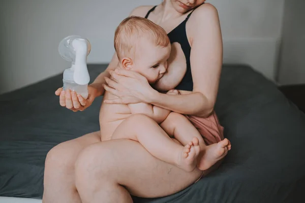 Madre joven con bebé recién nacido lindo bebé desnudo, sosteniéndolo en los brazos, usando un extractor de leche abrazando y amamantando con leche materna. Niño sano, concepto de hospital y maternidad feliz. Vivero. —  Fotos de Stock