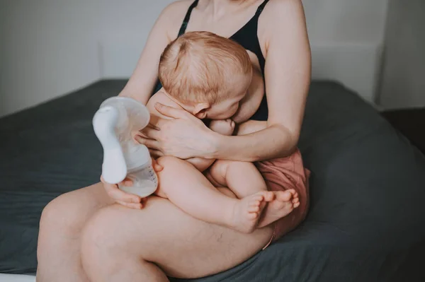 Young mother with newborn cute infant naked baby boy, holding him on arms, using breast pump hugging and breastfeeds with breast milk. Healthy child, concept of hospital and happy motherhood. Nursery. — Stock Photo, Image