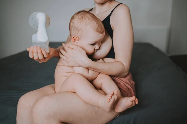 Young mother with newborn cute infant naked baby boy, holding him on arms, using breast pump hugging and breastfeeds with breast milk. Healthy child, concept of hospital and happy motherhood. Nursery. — Stock Photo, Image