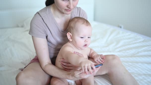 Petit bébé tout-petit garçon intéressé à regarder la mère qui travaille avec un téléphone intelligent. Enfant et technologie moderne. Famille heureuse se détendre dans la chambre tôt le matin. — Video