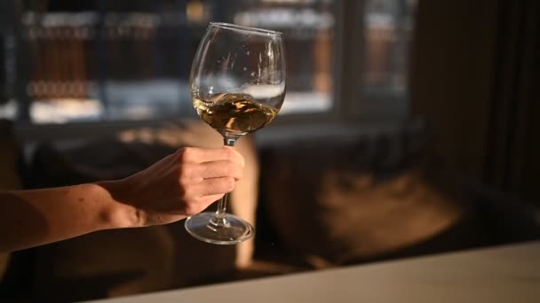 Маючи біле вино в склянці на жіночій руці. Розфокусований розмитий фон. Крупним планом повільне відео процесу змішування вина всередині чаші з сонячним світлом — стокове відео