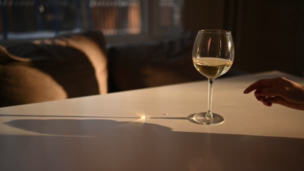 Ženské ruce cinkají sklenicemi se suchým bílým vínem na bílém stole. Rozostřené rozmazané pozadí. Zavřít zpomalené video procesu míchání vína v poháru se slunečním světlem — Stock video
