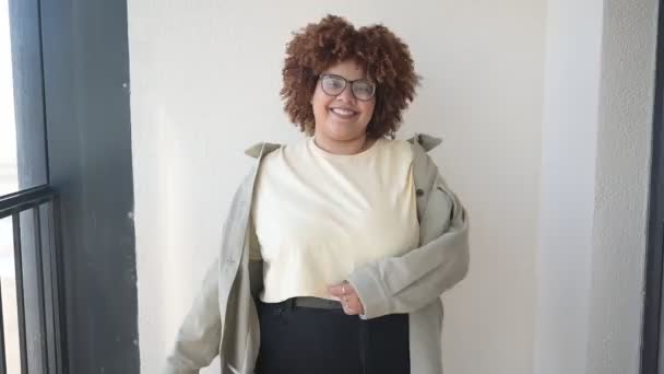 Mooie vrolijke glimlach ronding plus size Afrikaanse zwarte vrouw afro haar poseren in beige t-shirt, jeans, stijlvolle bril op zonnig balkon. Lichaamsimperfectie, acceptatie lichaam positief diversiteitsconcept — Stockvideo