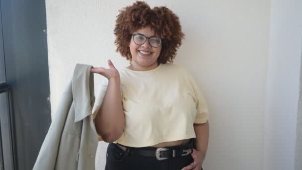 Mooie vrolijke glimlach ronding plus size Afrikaanse zwarte vrouw afro haar poseren in beige t-shirt, jeans, stijlvolle bril op zonnig balkon. Lichaamsimperfectie, acceptatie lichaam positief diversiteitsconcept — Stockvideo