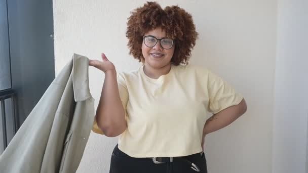 Bella felice sorridente curvy plus size africana donna nera afro capelli in posa in beige t-shirt, jeans, occhiali alla moda sul balcone soleggiato. Corpo imperfezione, accettazione corpo concetto di diversità positiva — Video Stock