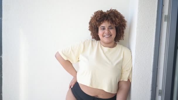 Vacker glad kurvig plus storlek afrikansk svart kvinna afro hår poserar i beige t-shirt och svarta underkläder på solig balkong. Kroppslig ofullkomlighet, kroppens acceptans, kroppspositivt och mångfaldskoncept — Stockvideo
