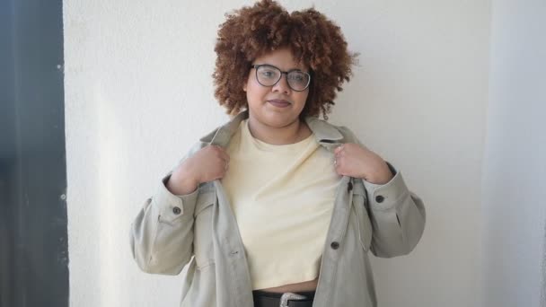 Hermosa feliz sonrisa curvas más el tamaño Africano negro mujer afro pelo posando en camiseta beige, jeans, gafas con estilo en el balcón soleado. Imperfección corporal, aceptación cuerpo concepto de diversidad positiva — Vídeos de Stock