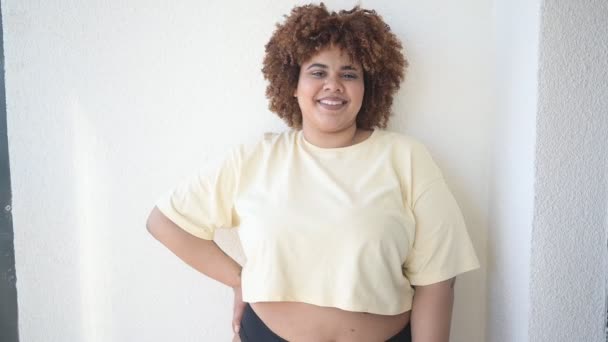 Hermosa curvas feliz más el tamaño Africano negro mujer afro pelo posando en camiseta beige y ropa interior negra en el balcón soleado. Imperfección corporal, aceptación corporal, concepto de cuerpo positivo y diversidad — Vídeos de Stock