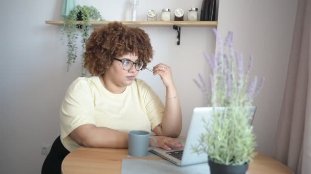 Attrayant heureux élégant plus la taille africaine femme noire étudiant afro cheveux dans des lunettes étudiant en ligne travaillant sur ordinateur portable à la maison espace de travail de bureau. La diversité. Travail à distance, enseignement à distance. — Video