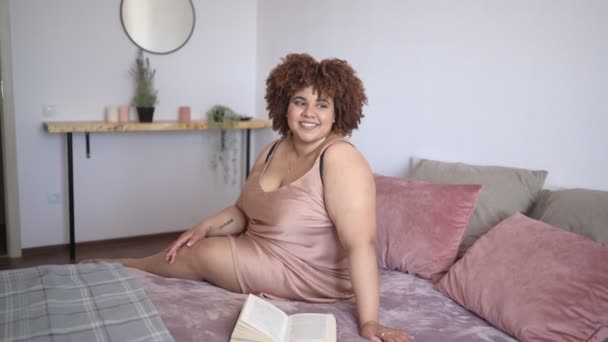 Belle courbure plus la taille africaine femme noire afro cheveux couchés sur le lit en soie robe rose poudre confortable chambre design intérieur. Imperfection corporelle, acceptation corporelle, corps positif et concept de diversité — Video