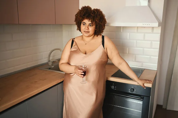 Bela curvilínea plus size Africano preto mulher afro cabelo bebendo vinho tinto no moderno estilo escandinavo cozinha design de interiores. Imperfeição corporal, aceitação corporal, corpo positivo e conceito de diversidade — Fotografia de Stock