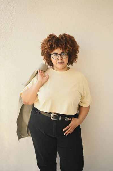 Bonita feliz sorrindo curvy plus size Africano preto mulher afro cabelo posando bege t-shirt, jeans, óculos elegantes no fundo bege. Imperfeição corporal, aceitação corpo conceito diversidade positiva — Fotografia de Stock