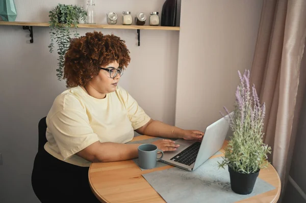 Menarik bahagia gaya ditambah ukuran Afrika perempuan kulit hitam mahasiswa afro rambut dalam gelas belajar online bekerja pada komputer laptop di ruang kerja rumah. Keragaman. Pekerjaan jarak jauh, pendidikan jarak jauh. — Stok Foto