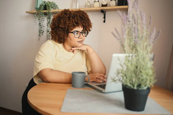 Attractive happy stylish plus size African black woman student afro hair in glasses studying online working on laptop computer at home office workspace. Diversity. Remote work, distance education. Stock Image