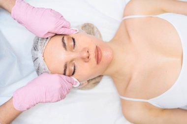 Güzel, mutlu bir kadın spa tedavisi görüyor. Güzellik salonundaki kozmetik uzmanı kozmetik süngerlerle kadının yüzünü temizliyor. Yüz güzelliği. Mükemmel temiz bir cilt. Gençlik ve cilt bakımı kavramı 