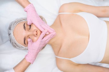 Eldivenli güzellik uzmanları genç bir kadının yüzüne dokunuyor. Estetik ameliyat konsepti. Yüz güzelliği ve masaj. Mükemmel makyajlı ve yumuşak tenli güzel sarışın kadın portresi.. 