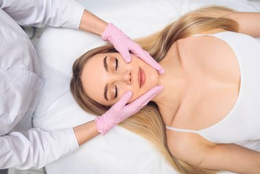 Eldivenli güzellik uzmanları genç kadınların yüzüne dokunuyor. Estetik ameliyat konsepti. Yüz güzelliği. Mükemmel makyajlı ve yumuşak tenli güzel sarışın kadın portresi.