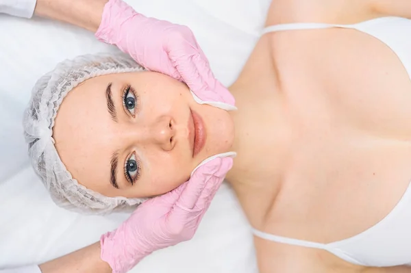 Güzel, mutlu bir kadın spa tedavisi görüyor. Güzellik salonundaki kozmetik uzmanı kozmetik süngerlerle kadının yüzünü temizliyor. Yüz güzelliği. Mükemmel temiz bir cilt. Gençlik ve cilt bakımı kavramı 