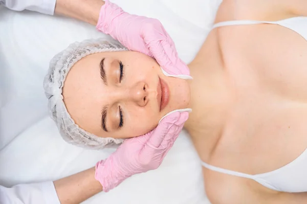 Hermosa mujer feliz recibiendo tratamiento de spa. Cosmetólogo en salón de belleza limpiando la cara de las mujeres con esponjas cosméticas. Belleza facial. Piel limpia fresca perfecta. Concepto de juventud y cuidado de la piel. — Foto de Stock