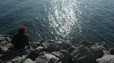Arka manzara artı Afrikalı zenci kadın afro saçı gün batımında huzurlu bir deniz kenarında tatilin tadını çıkarıyor güneşli hava, kayalar, mavi okyanus suyu. Vücut pozitif çeşitlilik kavramı