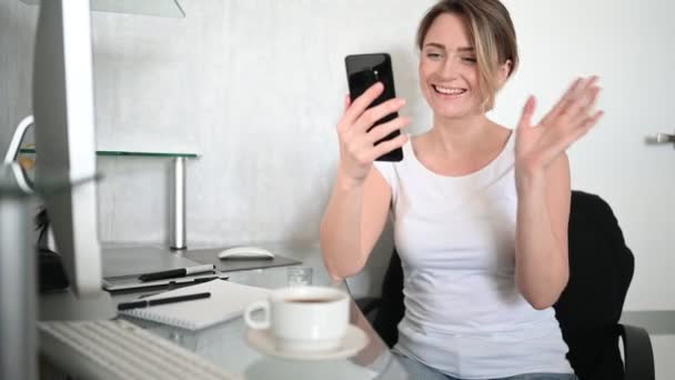 기술, 비디오 콘퍼런스, 가상 이벤트 개념 - 행복 한 젊은 여성 이 가정 사무실 사무실에서 컴퓨터 앞에 앉아 스마트폰으로 셀카나 비디오 통화를 하며. — 비디오