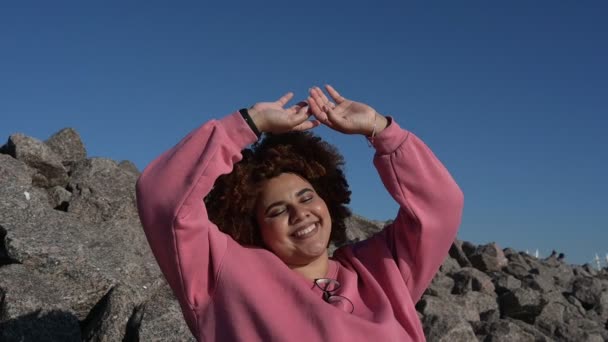 Vacker glad leende plus storlek afrikansk svart kvinna afro hår i rosa hoody utanför njuter av ljust soligt väder och blå himmel. Kroppslig ofullkomlighet, acceptans kropp positiv mångfald koncept — Stockvideo