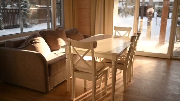 Leichtes Interieur des Wohnzimmers Landhaus im skandinavischen Stil. Panoramafenster, weißer Esstisch mit Stühlen, gemütliches beiges Sofa. Winterlandschaft vor dem Fenster. — Stockvideo