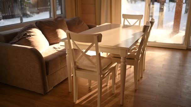 Projeto interior leve da casa de madeira do país da sala de estar no estilo escandinavo. Janelas panorâmicas, mesa de jantar branca e cadeiras, sofá bege aconchegante. Paisagem de inverno fora da janela. — Vídeo de Stock