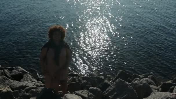 Happy plus size Afrikaanse zwarte vrouw afro haar buiten genieten 's avonds vakantie aan zee bij zonsondergang, zonnig weer, rotsen, blauwe oceaan water. Lichaamsimperfectie, acceptatie lichaam positief diversiteitsconcept — Stockvideo