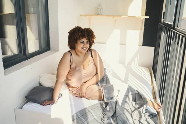 Indah melengkung ditambah ukuran Afrika hitam wanita afro rambut di tempat tidur dengan selimut kotak-kotak abu-abu nyaman kamar tidur cerah balkon. Sinar matahari. Ketidaksempurnaan tubuh, penerimaan tubuh, tubuh konsep positif dan keragaman — Stok Foto