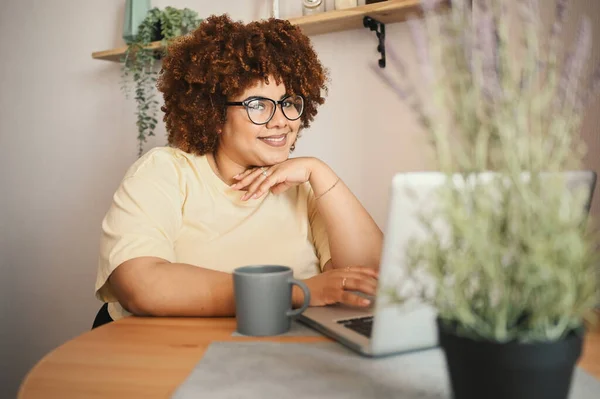 Attractive happy stylish plus size African black woman student afro hair in glasses studying online working on laptop computer at home office workspace. Diversity. Remote work, distance education. Stock Photo