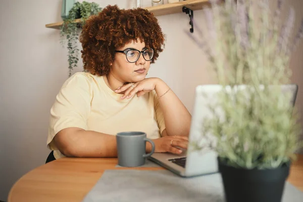 Menarik bahagia gaya ditambah ukuran Afrika perempuan kulit hitam mahasiswa afro rambut dalam gelas belajar online bekerja pada komputer laptop di ruang kerja rumah. Keragaman. Pekerjaan jarak jauh, pendidikan jarak jauh. Stok Foto Bebas Royalti