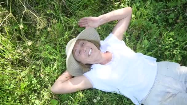 Felice sorridente anziana donna anziana in cappello di paglia sdraiata sull'erba che soffre di insetti zanzare in giardino estivo vista dall'alto. Agricoltura, giardinaggio, agricoltura, pensionati. — Video Stock