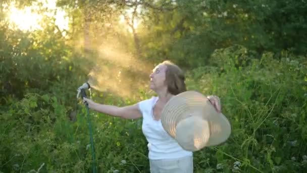 Mulher idosa feliz sênior se divertindo regando plantas com mangueira no jardim de verão. Gotas de água em luz de fundo. Agricultura, jardinagem, agricultura, pessoas de idade avançada. Cultivo de produtos hortícolas biológicos na exploração agrícola — Vídeo de Stock