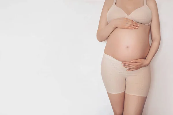 Невпізнавана молода вагітна жінка позує в бежевій компресійній білизні для схуднення, ізольованій на білому. Активний майбутній маминий спосіб життя. Концепція здорової вагітності материнства. Вільний простір для тексту . — стокове фото