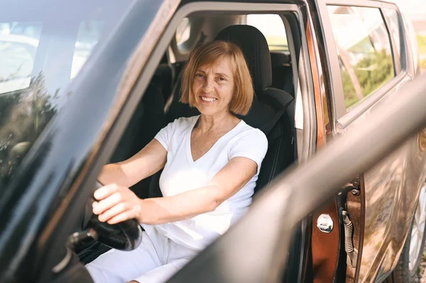 Wanita tua yang bahagia duduk di mobil coklat baru, tersenyum sambil melihat kamera menikmati perjalanan. Mengemudi kursus dan konsep asuransi jiwa. Pensiunan konsep aktivitas orang. — Stok Foto