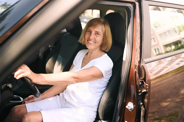 Happy senior woman driving sitting in new brown car, smiling looking at camera enjoying journey.Driving courses and life insurance concept. Retired people activity concept.