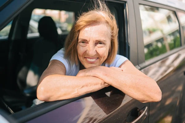 Wanita tua yang bahagia duduk di mobil coklat baru, tersenyum sambil melihat kamera menikmati perjalanan. Mengemudi kursus dan konsep asuransi jiwa. Pensiunan konsep aktivitas orang. — Stok Foto