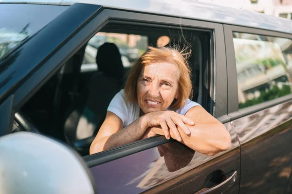 Glückliche Seniorin im neuen braunen Auto sitzend, lächelnd in die Kamera blickend, genießt die Gesellen.Fahrkurse und Lebensversicherungskonzept. Seniorenaktivitätskonzept. — Stockfoto