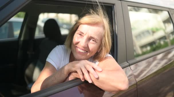 Bonne femme âgée conduisant assis dans une nouvelle voiture brune, souriant en regardant la caméra profiter du voyage.Cours de conduite et concept d'assurance-vie. Concept d'activité des retraités. — Video