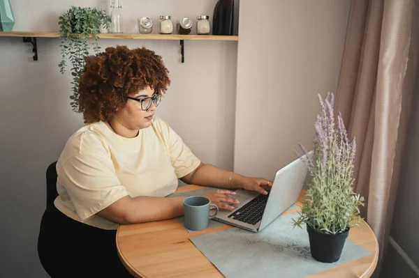 Atraktivní šťastný stylový plus velikost africké černošky studentka afro vlasy v brýlích studuje on-line pracuje na notebooku na domácím kancelářském pracovišti. Rozmanitost. Vzdálená práce, distanční vzdělávání. — Stock fotografie