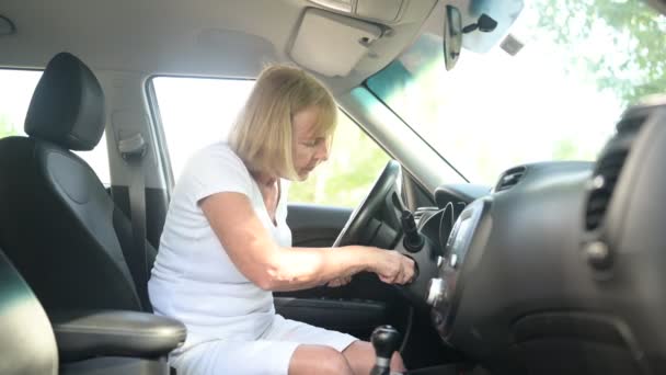 Mujer mayor conduciendo sentada en un coche nuevo, usando cinturones de seguridad, preparándose para el primer viaje, enojada porque no puede arrancar el motor. Concepto de actividad para jubilados. — Vídeo de stock